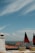 A scenic view with rooftops of orange tiles and historic buildings overlooking a large body of water under a sky with scattered clouds. In the foreground, there are small model trams adorned with Portuguese flags.