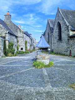 A cozy medieval village scene from the Minecraft server with players interacting near a stone well.