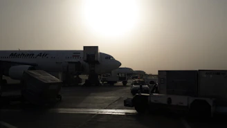 An airplane taking off at sunrise with cargo loading activity in the foreground.
