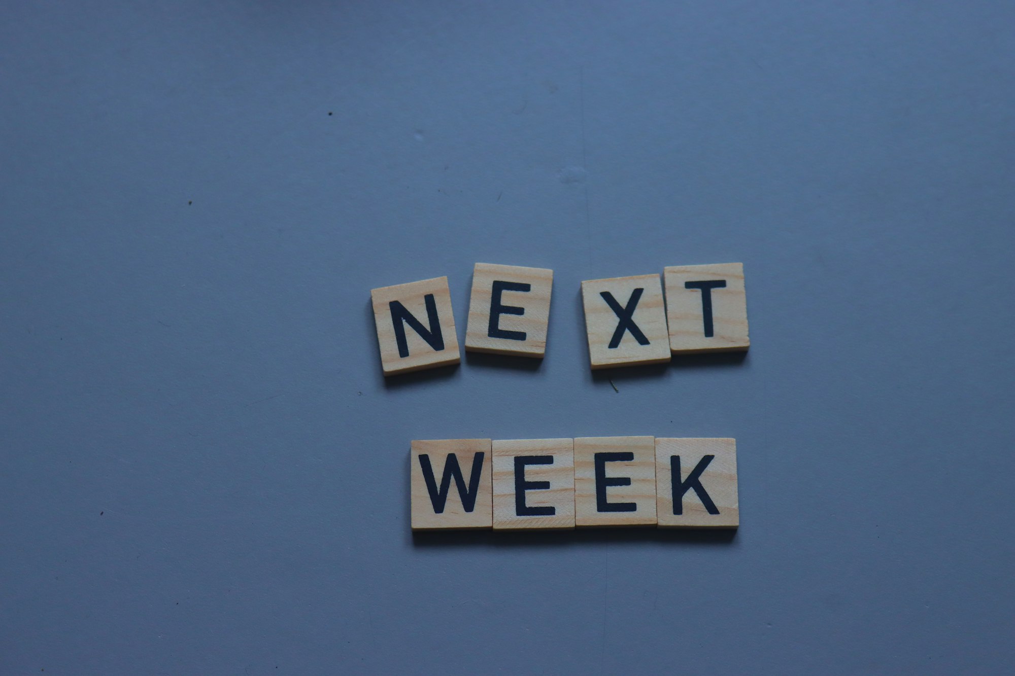 scrabble tiles spelling the word next week on a blue background