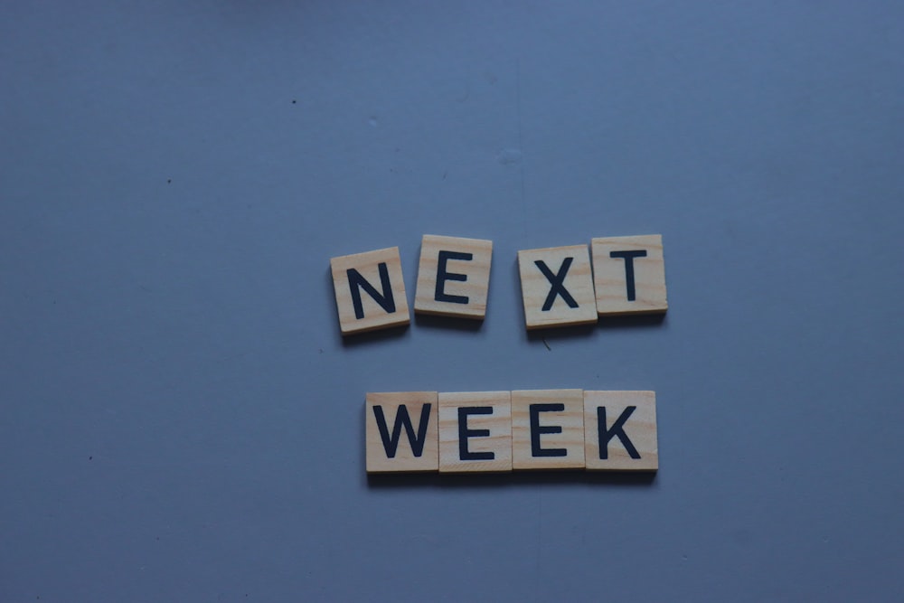 Scrabble Tiles soletrando a palavra na próxima semana em um fundo azul