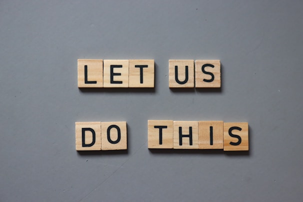 Wooden tiles with black letters spell out the motivational phrase 'LET US DO THIS' arranged on a gray background.