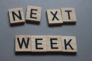 Wooden letter tiles spelling out the words 'NEXT WEEK' arranged on a flat surface.