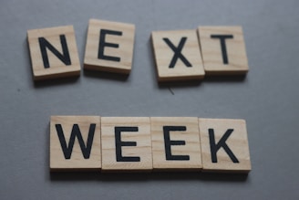 Wooden letter tiles spelling out the words 'NEXT WEEK' arranged on a flat surface.