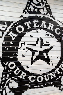 The image depicts a bold mural painted on a panel with large text and a central star emblem. The words 'Aotearoa' and 'Our Country' are prominently displayed in white against a black background, suggesting a strong cultural or national theme.