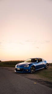 Electric blue sports car gleaming on a coastal highway at sunset.