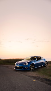Electric blue sports car gleaming on a coastal highway at sunset.