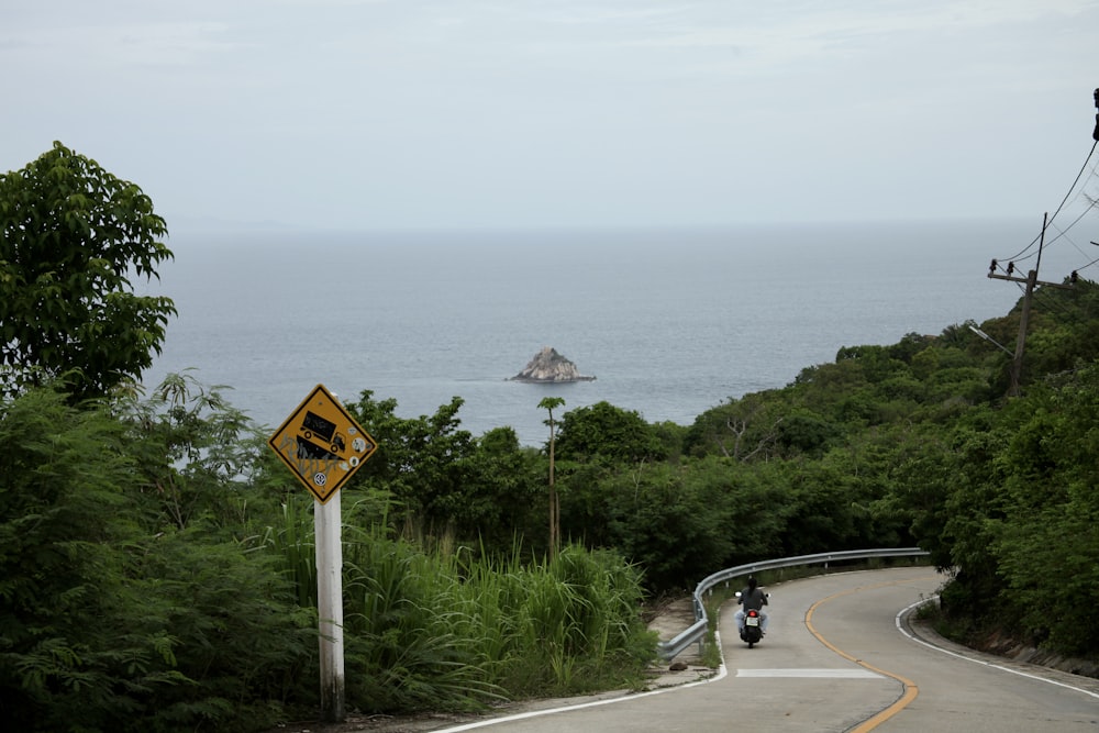 uma pessoa andando de moto por uma estrada ao lado do oceano