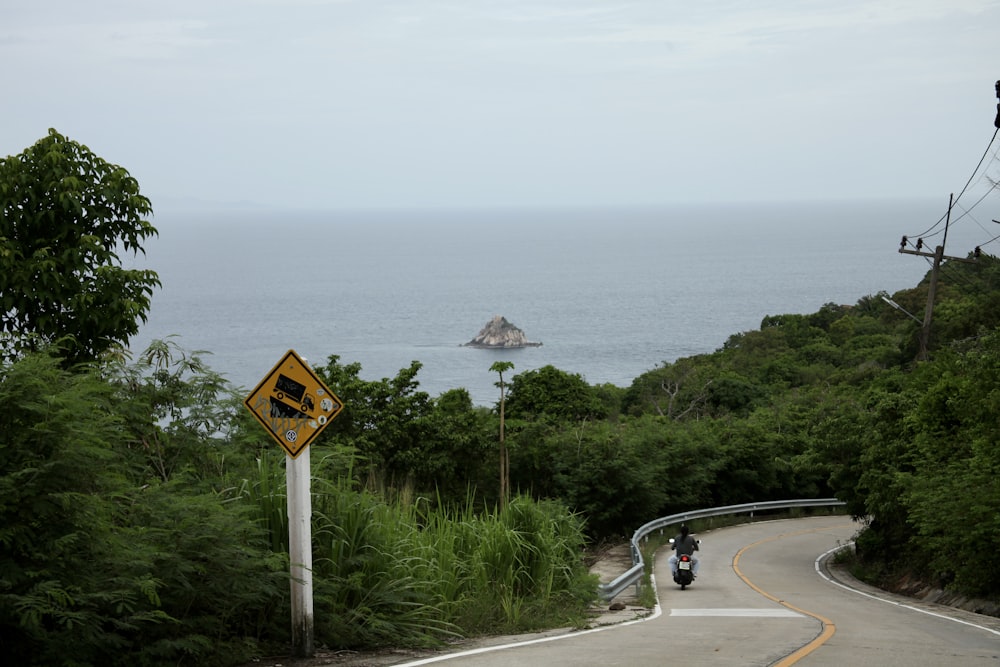 a person riding a motorcycle down a road next to the ocean