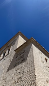 A detailed view of an ornate brick building with intricate stonework against a clear blue sky. The structure features small windows and decorative elements, emphasizing architectural craftsmanship.