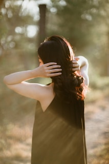 A hand gently applying rosemary hair oil to long, healthy hair in natural sunlight.