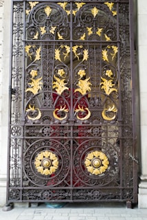 A sturdy red iron gate with intricate scrollwork, set against a lush garden backdrop.