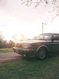 A vintage car parked beside a weathered barn, bathed in warm, late afternoon light.