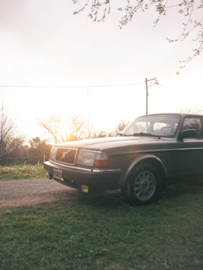 A vintage car parked beside a weathered barn, bathed in warm, late afternoon light.