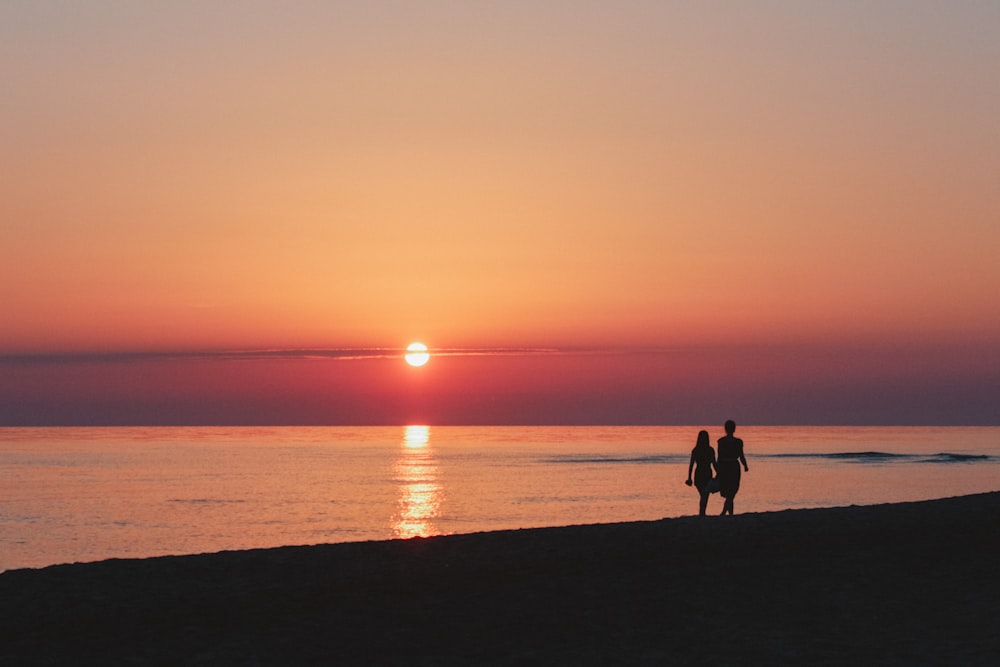 two people walking on a beach at sunset