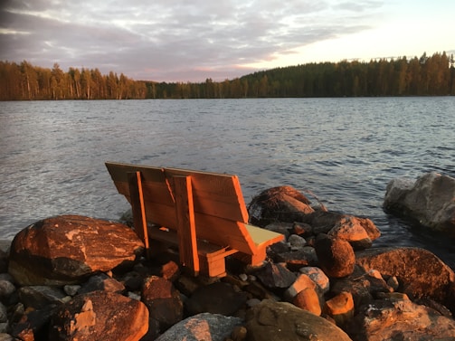 An empty bench overlooking a calm lake during sunset.