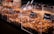 A variety of nuts and dried fruits are displayed in transparent containers at a market or store. Each section is labeled with its specific mix, and metal scoops are placed on the side for serving. The selection includes almonds, raisins, and other mixed nuts.