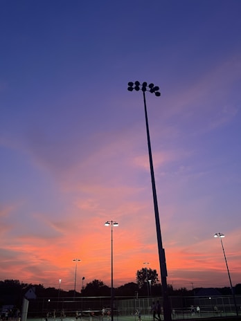 Sunset over a lively padel court with players mid-match and cheers in the background.