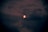 A red moon partially obscured by dark clouds in a night sky, creating an eerie and mystical atmosphere.