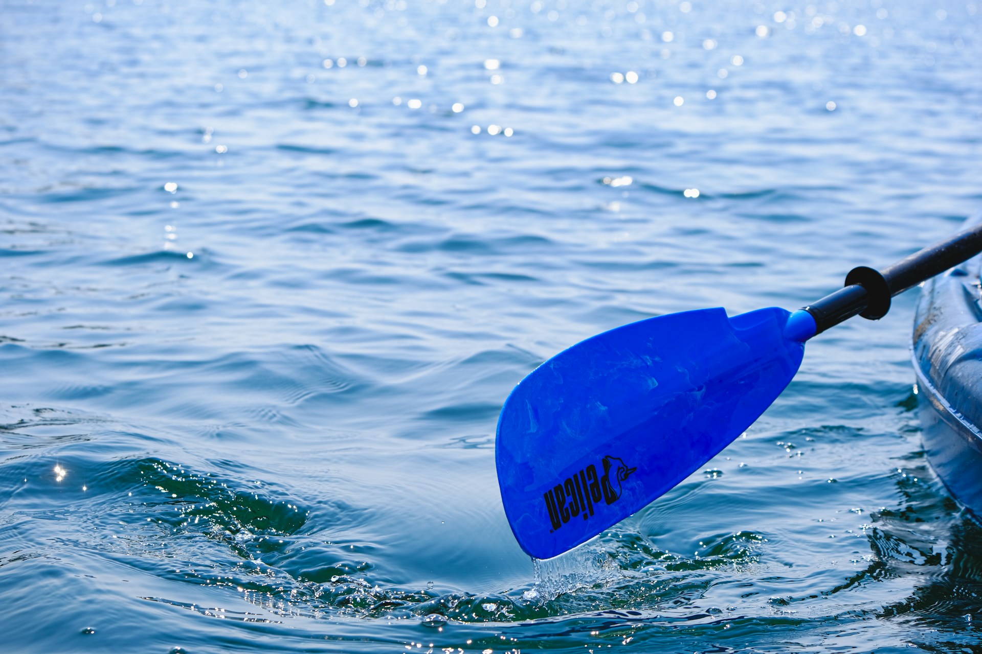 Close-up of a paddle slicing through crystal-clear water, droplets sparkling in the sunlight during a peaceful lake adventure.