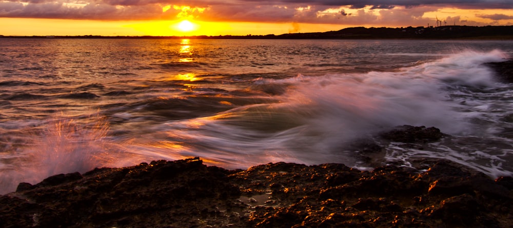 a sunset over the ocean with waves crashing on the rocks