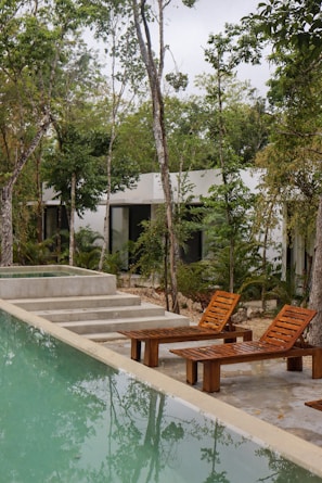 a couple of wooden chairs sitting next to a swimming pool