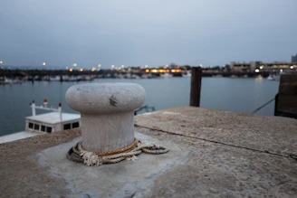 Close-up of a heavy-duty steel marine bollard firmly anchored on a weathered wooden pier under a cloudy sky.