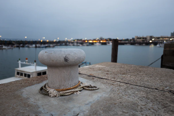 Close-up of a heavy-duty steel marine bollard firmly anchored on a weathered wooden pier under a cloudy sky.