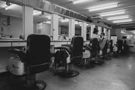A barbershop interior with several empty reclining chairs lined up along a mirrored wall.