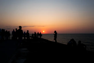 Sunset over the ocean with a silhouette of Gorée Island and peaceful gathering of people.