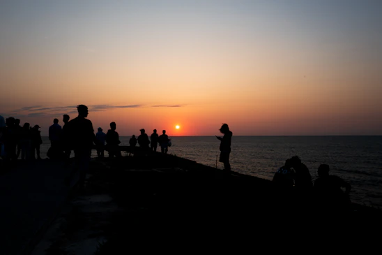 Sunset over the ocean with a silhouette of Gorée Island and peaceful gathering of people.