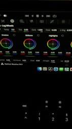 The image shows a computer screen displaying a video editing software interface, specifically DaVinci Resolve 18.5. Various color adjustment wheels for shadows, midtones, and highlights are visible, along with multiple control panels and icons at the top. A keyboard is partially visible at the bottom.