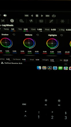 The image shows a computer screen displaying a video editing software interface, specifically DaVinci Resolve 18.5. Various color adjustment wheels for shadows, midtones, and highlights are visible, along with multiple control panels and icons at the top. A keyboard is partially visible at the bottom.
