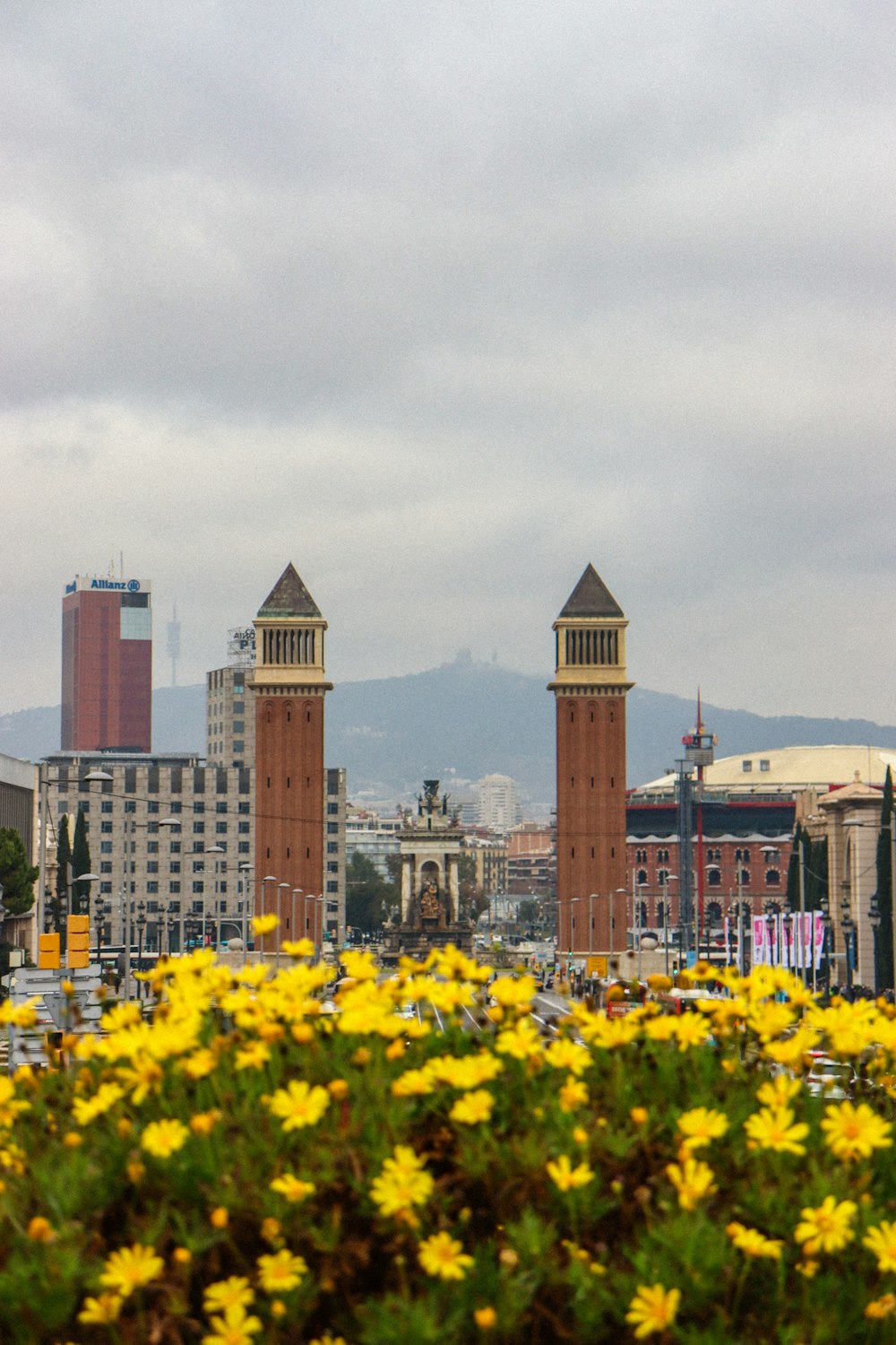 a view of a city with tall buildings and yellow flowers in the foreground