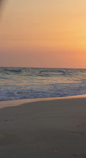 A serene beach at sunset with soft waves and vibrant orange skies, inviting relaxation.