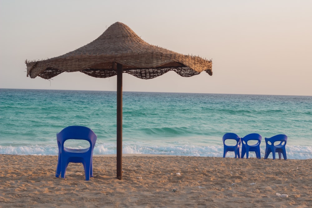 a couple of blue chairs sitting on top of a sandy beach