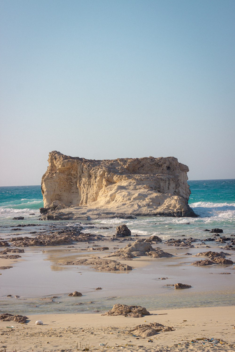 a large rock sticking out of the ocean next to a beach