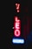 A neon sign glowing in the dark with the words 'VIDEO' and 'BOOKS'. The letters 'VIDEO' are vertically aligned in red, while 'BOOKS' is horizontally aligned in blue. The sign appears to be against a building facade.