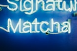 Bright neon sign spelling out 'Signature Matcha' against a vibrant blue background.