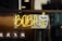 A neon sign featuring the word 'BOBA' in bright yellow letters, accompanied by a stylized image of a cup with bubbles, suggesting bubble tea. The sign is mounted on a window with darker background details.