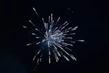 A dazzling fireworks burst lighting up the night sky over a festive outdoor concert.