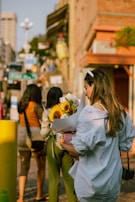 A smiling woman receiving a bouquet of flowers on a city street.