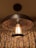 An industrial-style ceiling light fixture with an exposed bulb inside a metal cage, placed against a backdrop of damask-patterned curtains. The metal has a rustic, dark finish, giving the setting a warm and vintage look.