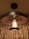An industrial-style ceiling light fixture with an exposed bulb inside a metal cage, placed against a backdrop of damask-patterned curtains. The metal has a rustic, dark finish, giving the setting a warm and vintage look.