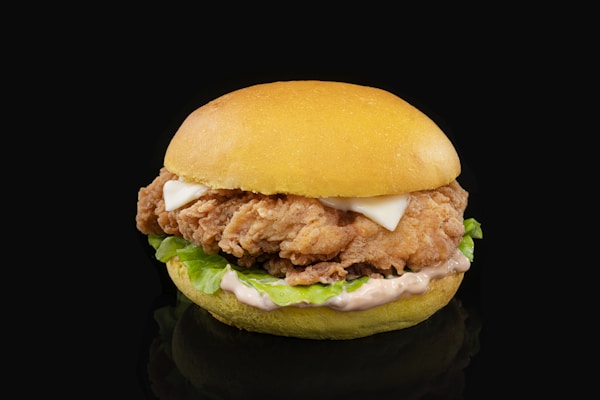 A chicken sandwich with lettuce and mayonnaise on a black background