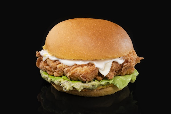 A chicken sandwich with lettuce and mayonnaise on a black background