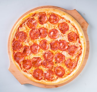 An overhead shot of a pepperoni pizza with crispy edges on a wooden board