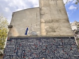 A large mural on the side of a building features a section of diverse languages with the phrase 'I love you' written in multiple scripts. Above this is a painted figure of a woman in a blue dress with an accompanying speech bubble.