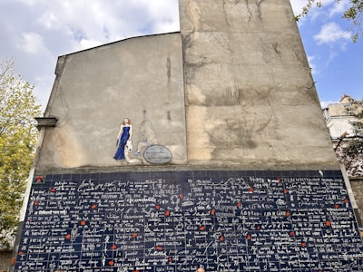 A large mural on the side of a building features a section of diverse languages with the phrase 'I love you' written in multiple scripts. Above this is a painted figure of a woman in a blue dress with an accompanying speech bubble.