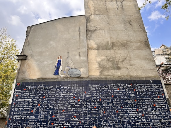 A large mural on the side of a building features a section of diverse languages with the phrase 'I love you' written in multiple scripts. Above this is a painted figure of a woman in a blue dress with an accompanying speech bubble.